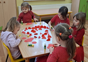 Pięć dziewczynek ozdabia białe serce czerwonymi kółeczkami, złożonymi na pół.